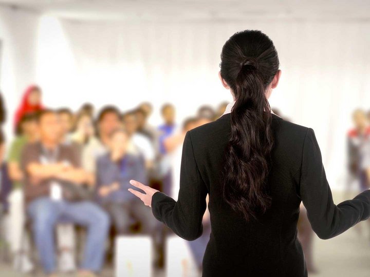 Успешный семинар. Девушка оратор. Выступающий перед аудиторией. Женщина проводит тренинг. Девушка выступает перед публикой.
